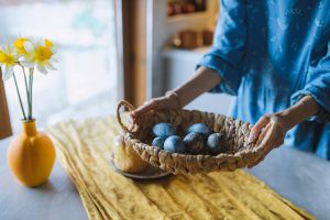 Easter Decorations Woman Placing a Wide Basket Filled with Colored Eggs on a Table